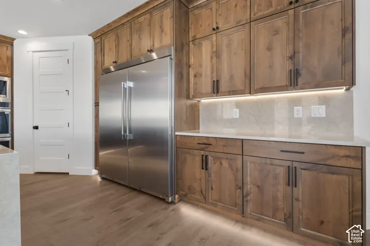 Kitchen featuring stainless steel refrigerator, wood cabinetry with dark hardware, under-cabinet lighting, and light-toned countertops