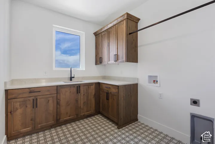 Laundry room featuring patterned tile flooring, wood-finish cabinetry, light-toned countertop, a window, and a built-in hanging rod