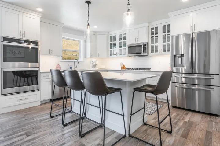 Modern kitchen featuring white cabinetry, stainless steel appliances, a center island with countertop seating, wood-finish flooring, and pendant lighting