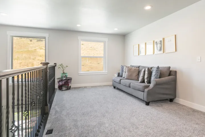 Carpeted loft area featuring two windows, recessed lighting, and a dark metal baluster railing