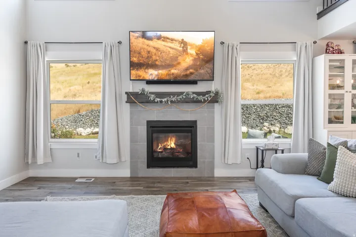 Living space featuring a stone-tile fireplace with a substantial wood mantel, flanked by two large windows