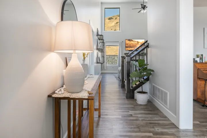 Inviting foyer with wood-finish flooring, a contemporary staircase featuring dark wood newel posts and black metal balusters, and expansive windows offering natural scenery