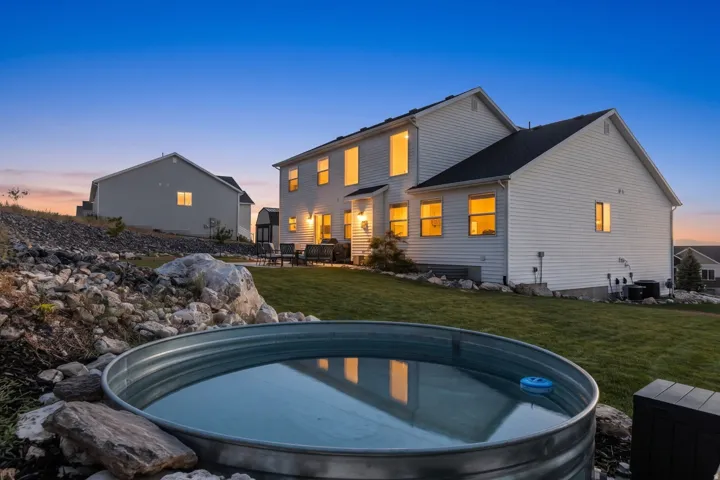 Expansive backyard featuring a circular metal stock tank, a rock-lined garden bed, and a sloped lawn