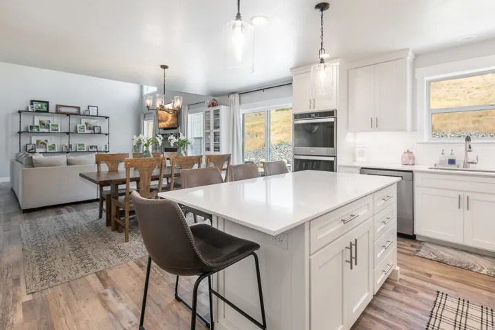Open-concept kitchen and living area featuring white cabinetry, a large kitchen island with a white countertop, stainless steel double wall ovens, and wood-finish flooring