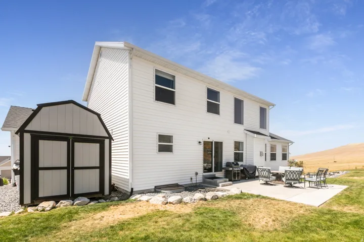 White siding exterior with a large concrete patio, sliding glass door access, and a detached shed featuring double doors