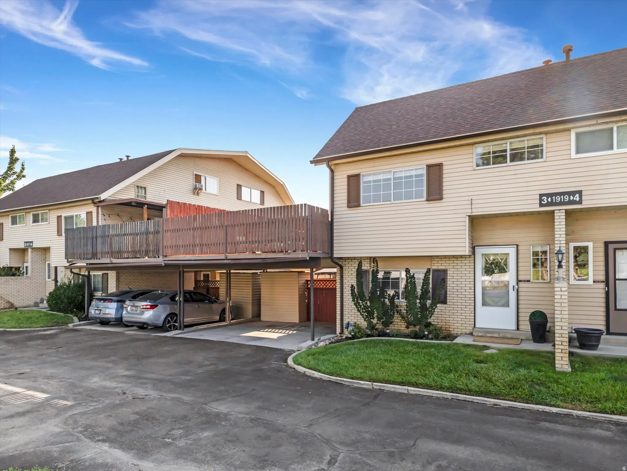Townhome exterior featuring tan siding, brick accents, brown shutters, and a covered carport with an upper-level balcony