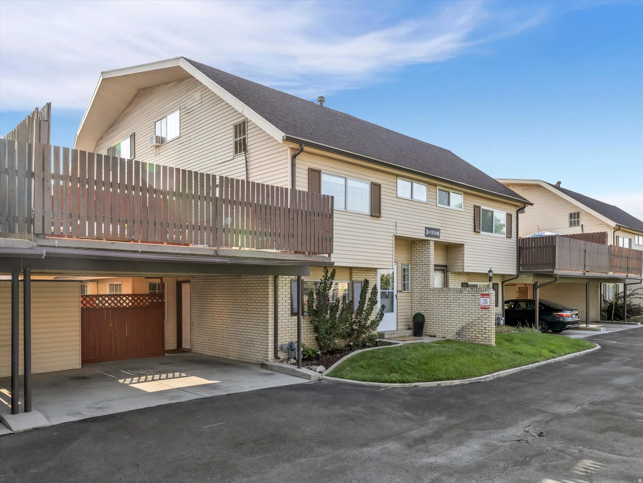 Townhome exterior featuring tan siding, dark brown shutters, and a dark shingle roof