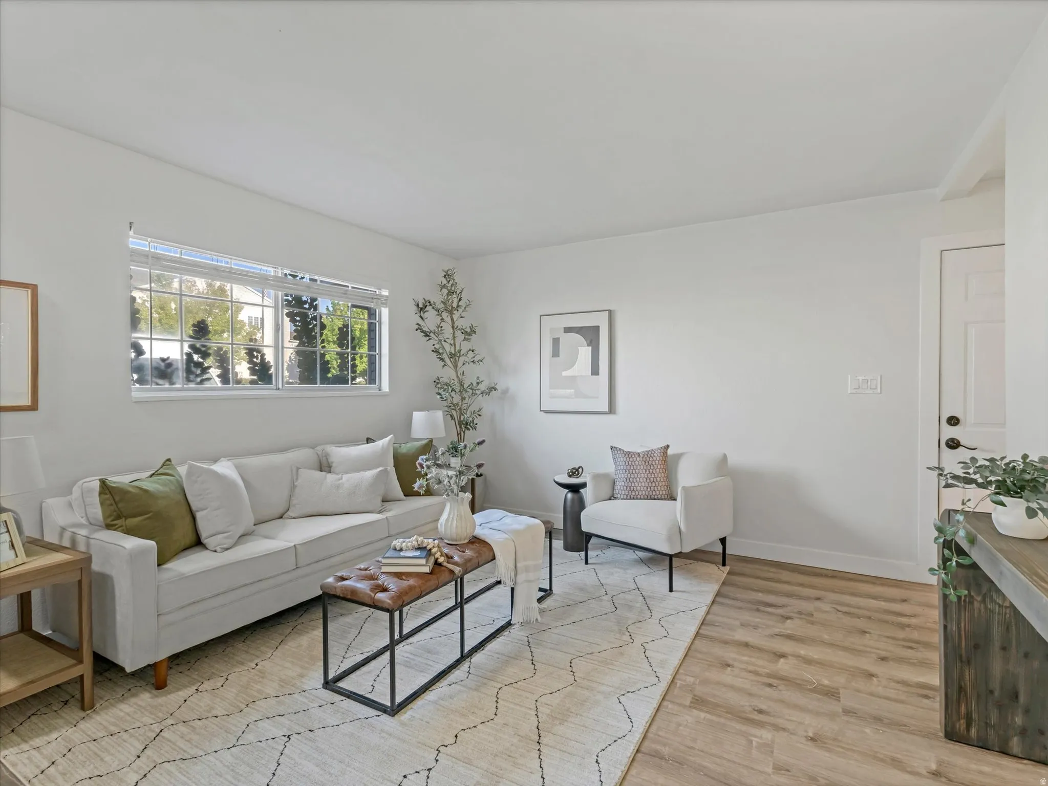 Bright living space featuring wood-finish flooring, white walls, and a large window with white blinds