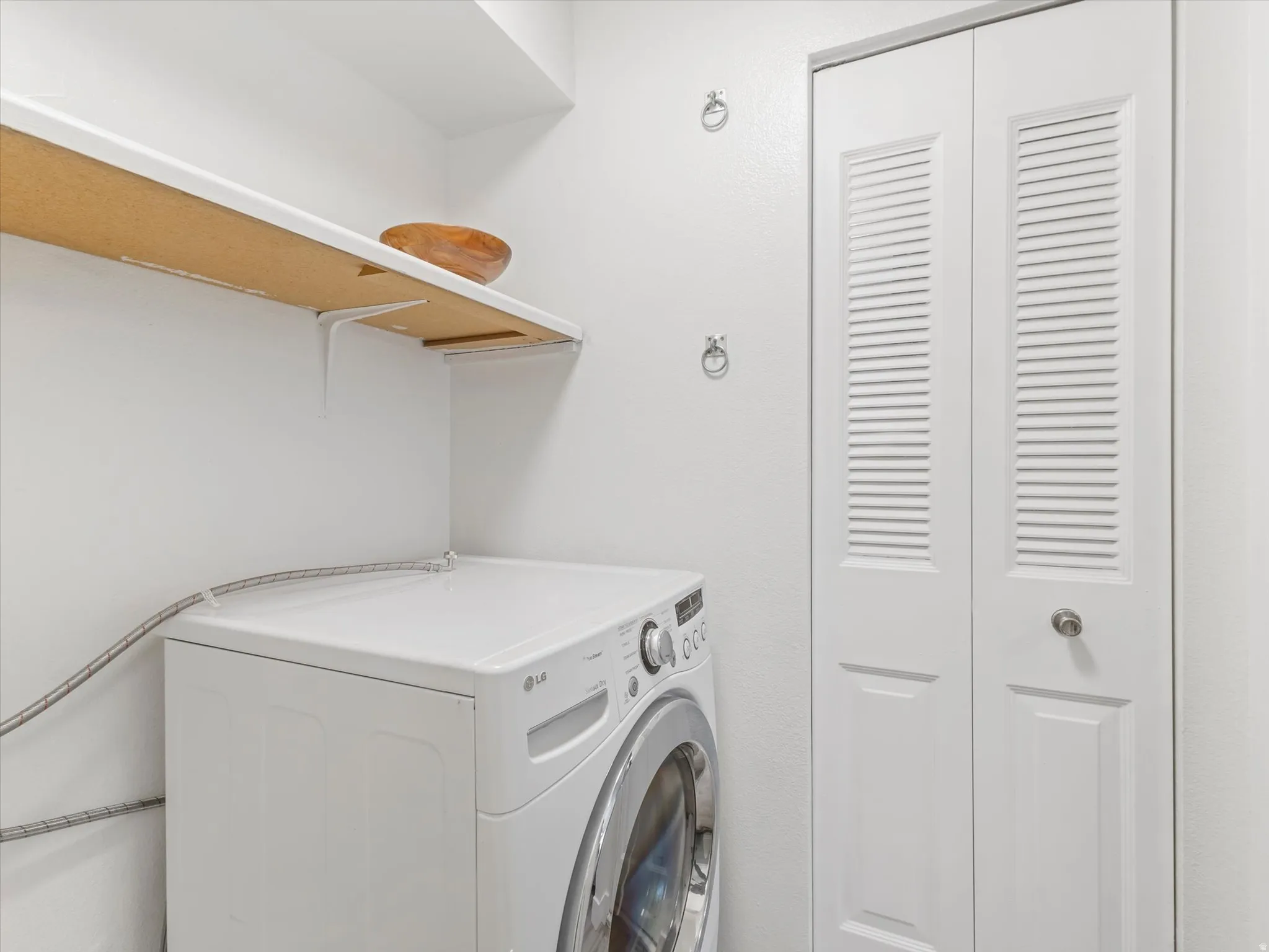 Laundry area with a built-in shelf, white walls, and a louvered bi-fold door