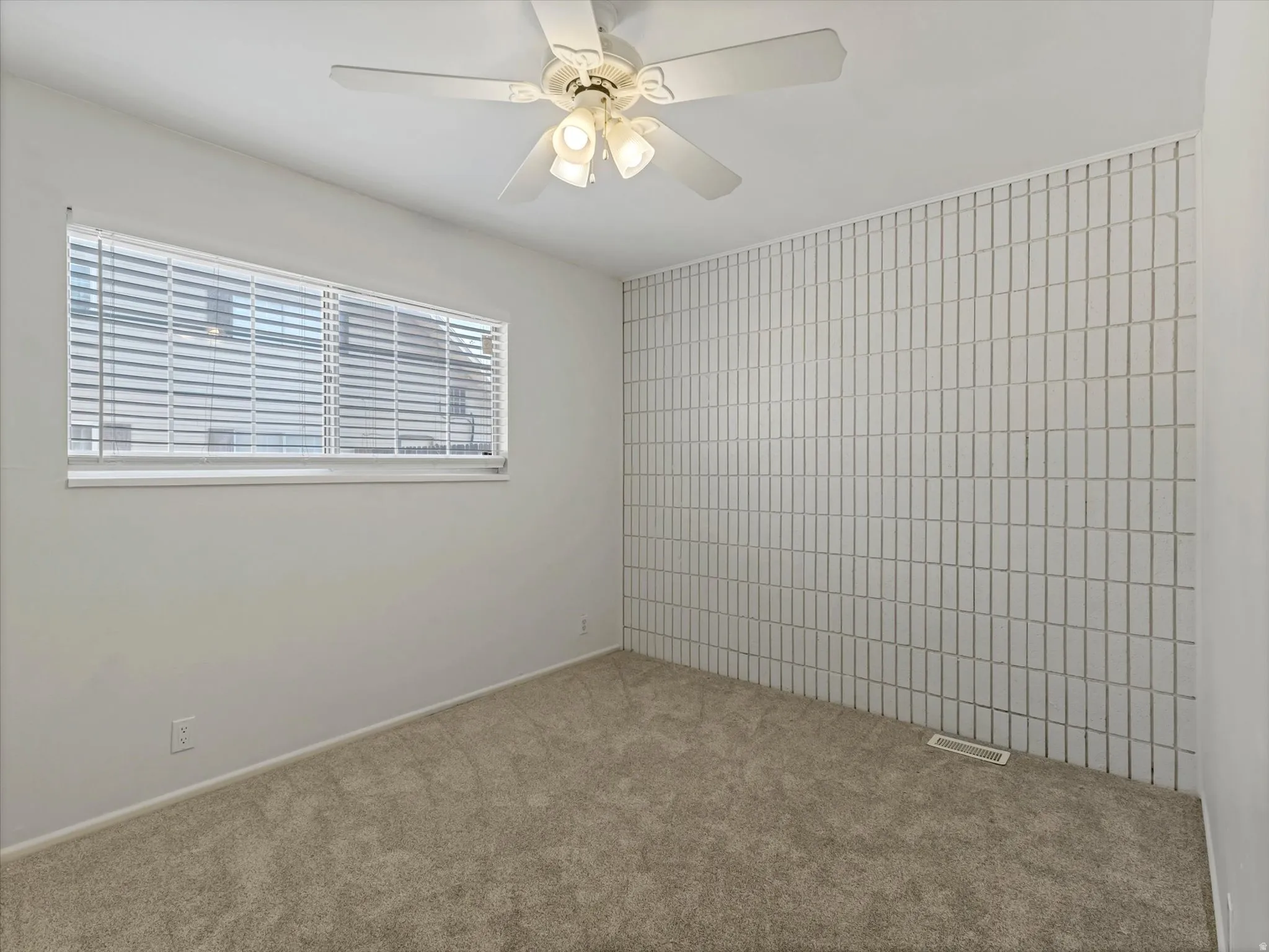 Room featuring textured wall paneling, light-colored carpet flooring, a horizontal window with blinds, and a ceiling fan with integrated lighting