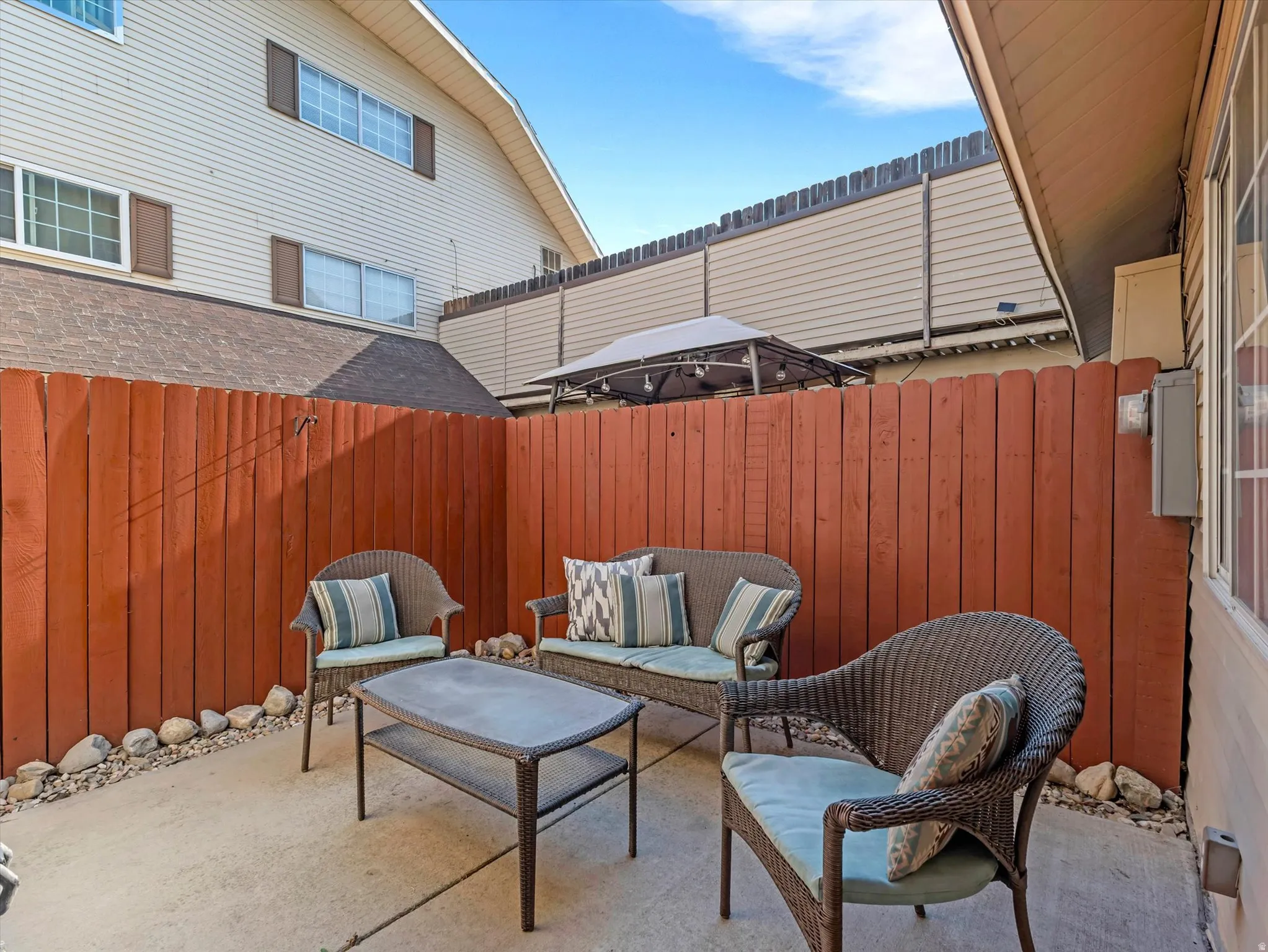 Private patio space featuring a concrete slab, red-stained vertical plank fencing, and decorative stone landscaping