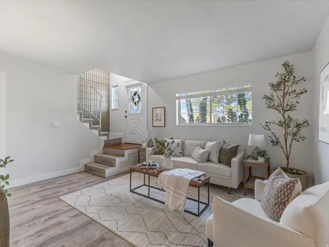 Open-concept living area featuring wood-finish flooring, a prominent window, white interior walls, and a staircase with a metal railing