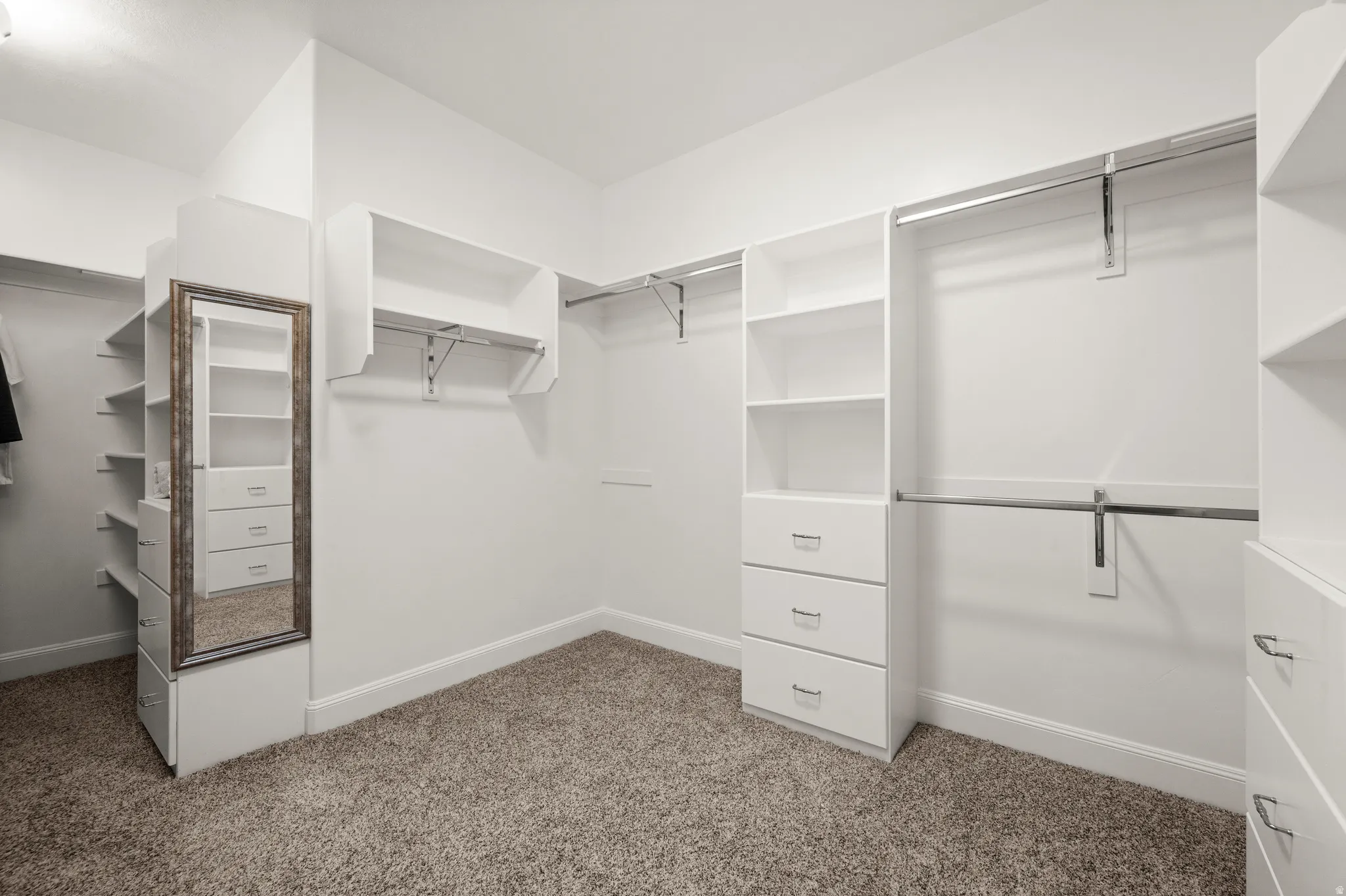Spacious walk-in closet featuring built-in shelving, multiple hanging rods, integrated drawers, and neutral carpet flooring