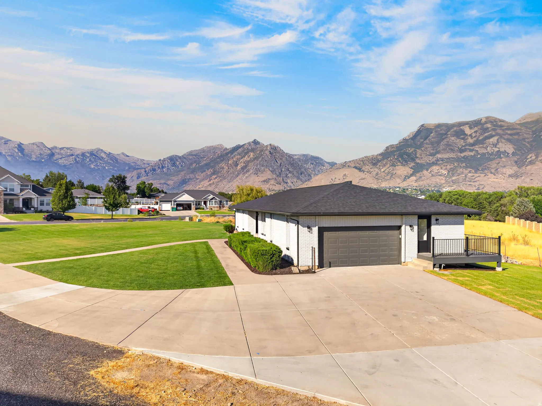 Contemporary single-story residence featuring a dark gray garage door, a front deck with black railings, and a wide concrete driveway