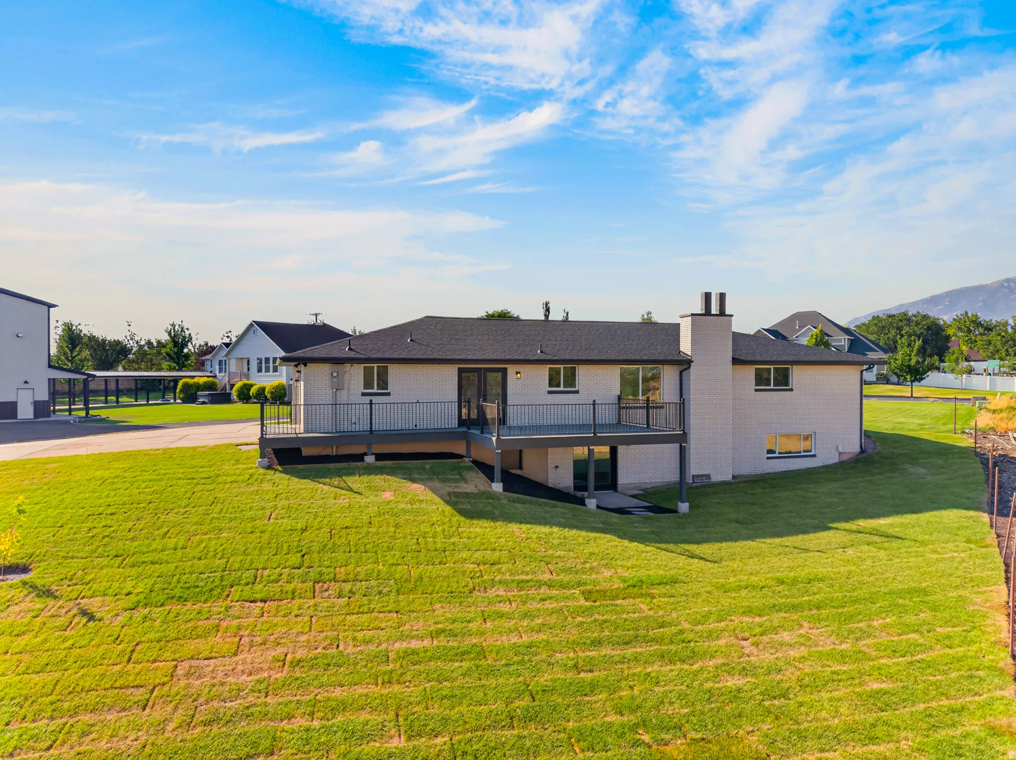 Rear exterior featuring a spacious deck with dark railing, a ground-level patio, and a sloped lawn
