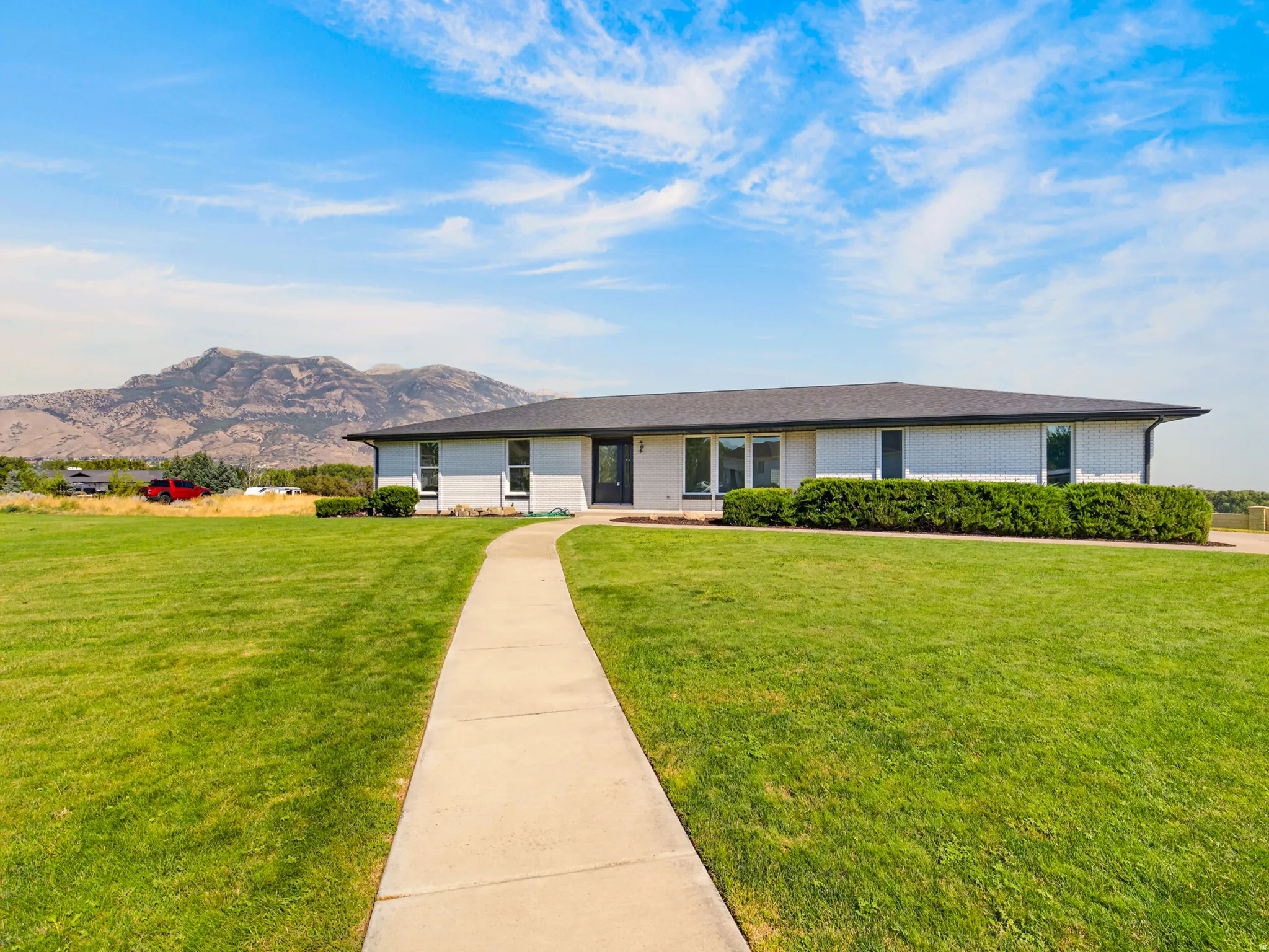 Ranch-style residence featuring a white brick facade, dark roofing, and a prominent concrete pathway