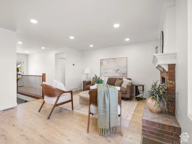 Light wood-finish flooring, recessed ceiling lighting, brick fireplace with decorative mantel, and a dark wood and metal railing