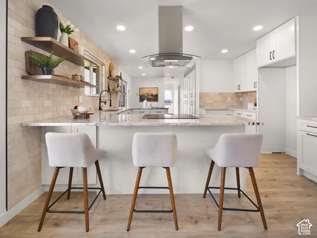 Kitchen featuring a center island, recessed lighting, wood-finish flooring, a stainless steel range hood, and white cabinetry