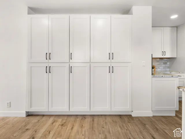 Extensive built-in white cabinetry with matte black hardware, wood-finish flooring, and a white backsplash with light-toned grout