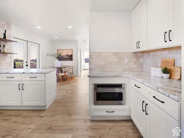 White shaker cabinetry, light-toned wood-finish flooring, stainless steel microwave, and light-toned backsplash