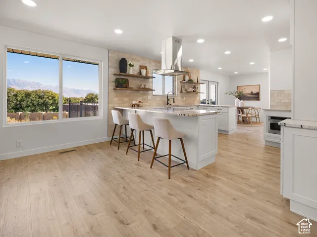 Bright kitchen with wood-finish flooring, white cabinetry, granite countertops, and a stainless steel range hood
