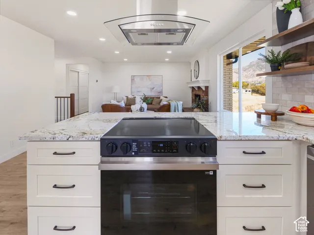 Kitchen island with light-toned countertop and integrated range, white cabinetry with dark pulls, and a stainless steel range hood