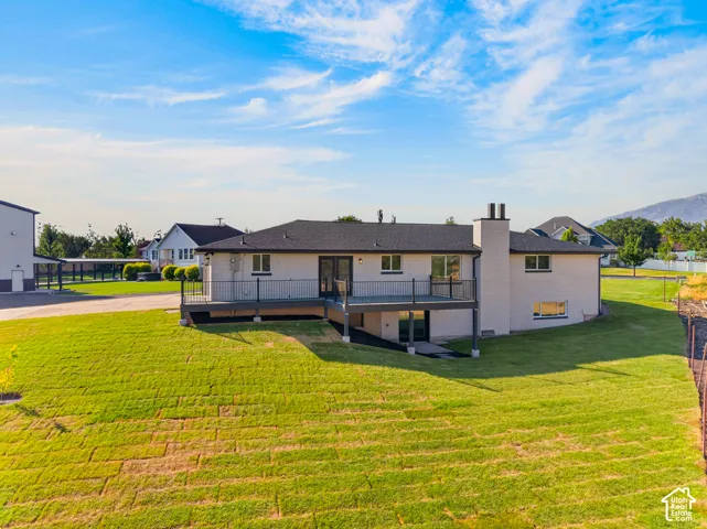 Rear exterior featuring a spacious deck with dark railing, a ground-level patio, and a sloped lawn