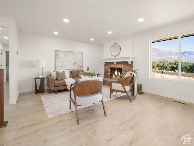 Light wood-finish flooring, brick fireplace with white mantel, recessed lighting, and large window
