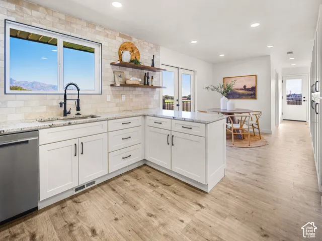 White shaker cabinetry, light-toned wood-finish flooring, recessed lighting, double French doors, and stone countertops