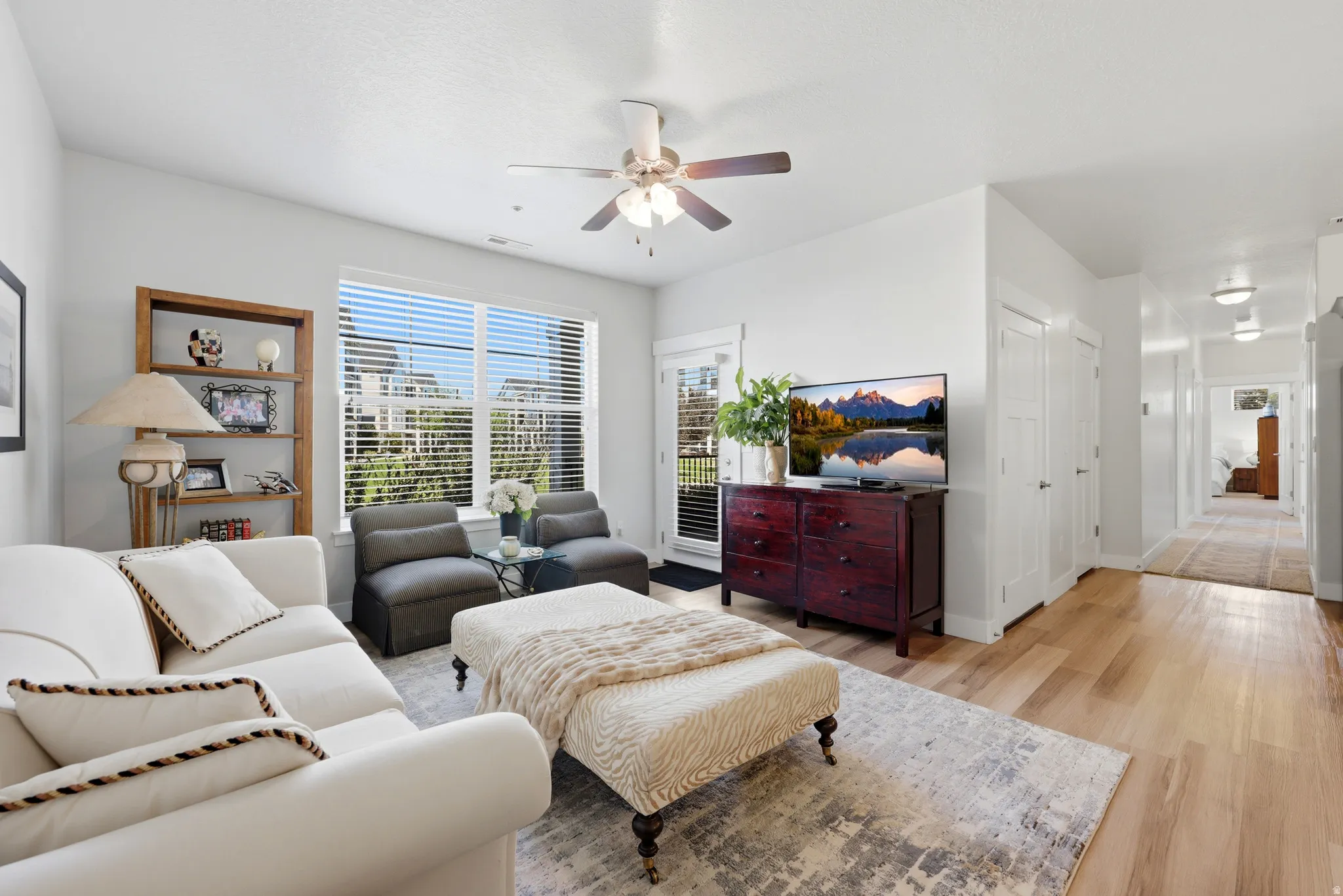 Living area featuring wood-finish flooring, a ceiling fan, and a large window with blinds