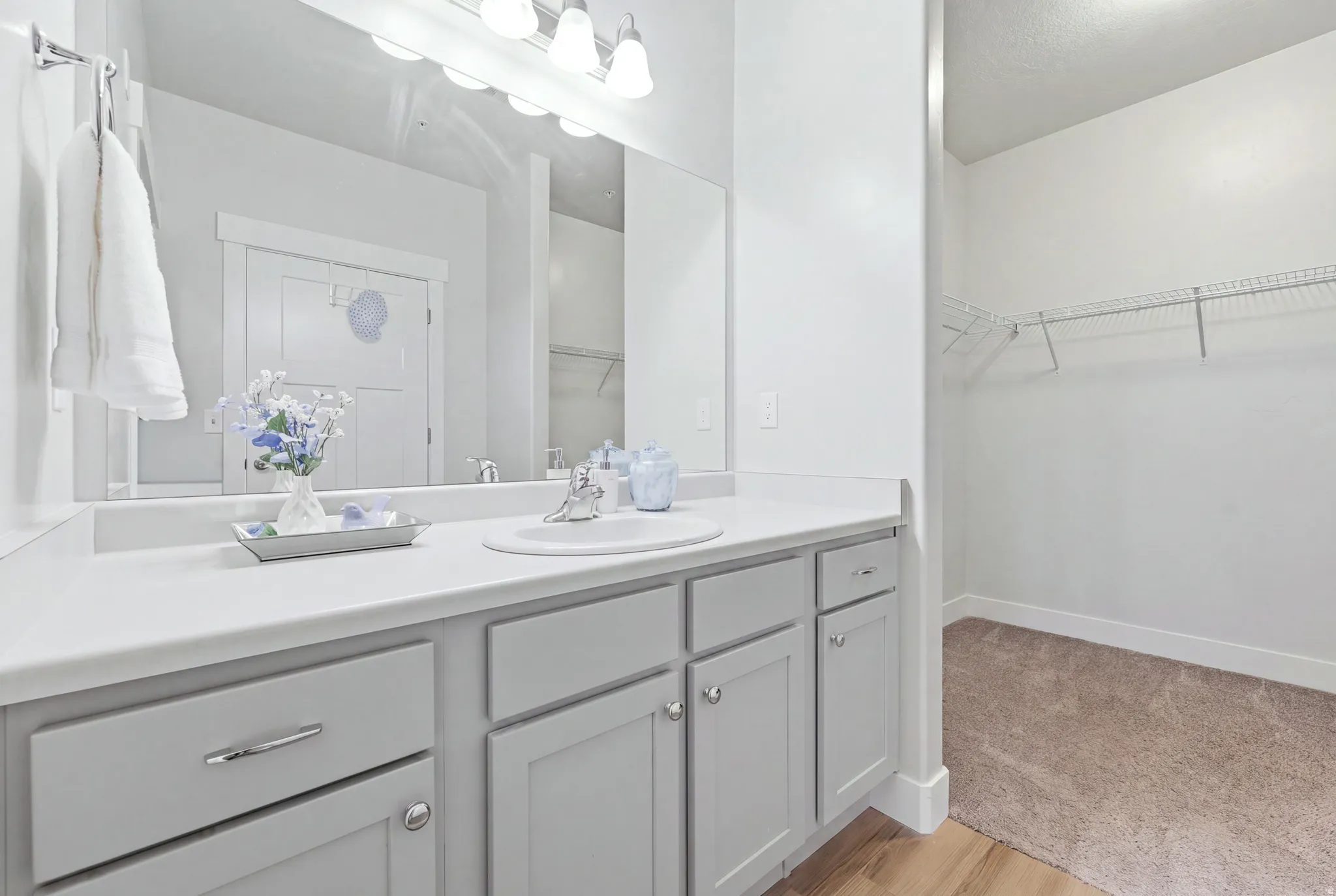 Bathroom vanity with a white countertop and light grey cabinetry, featuring a single sink with a chrome faucet
