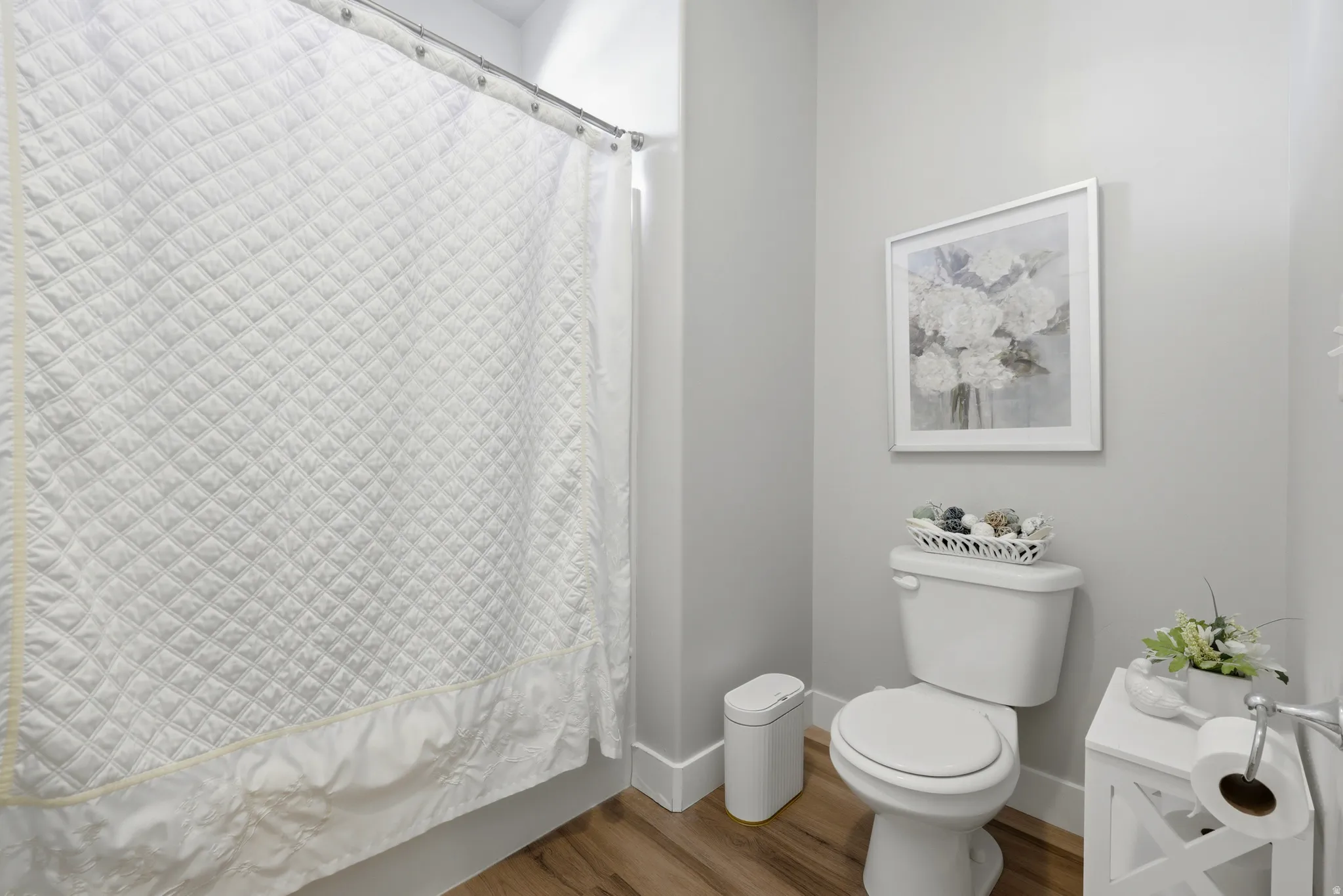 Bathroom featuring wood-finish flooring, a white toilet, and light gray walls
