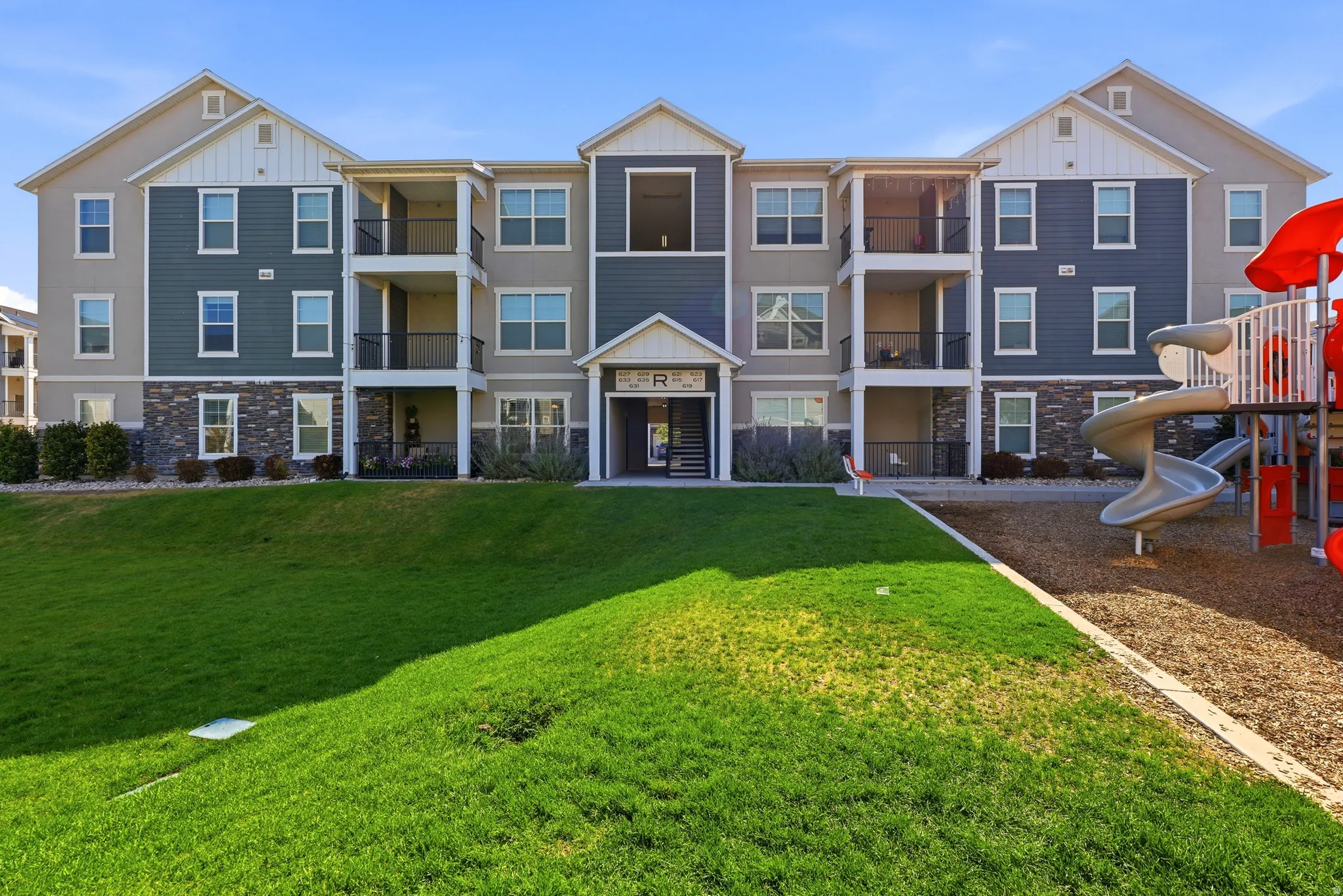 Multi-story apartment building featuring gabled rooflines, balconies, and stone veneer accents