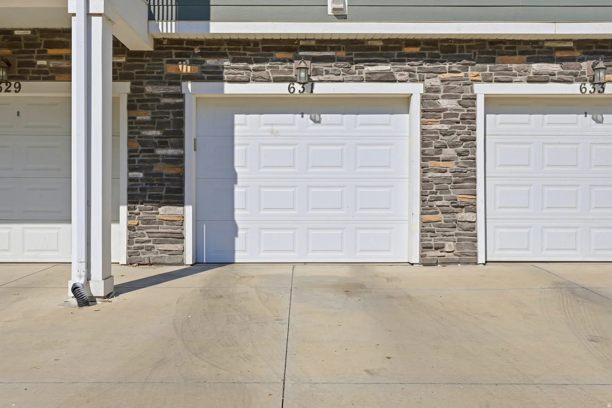 Individual garage doors featuring recessed paneling and exterior lighting fixtures