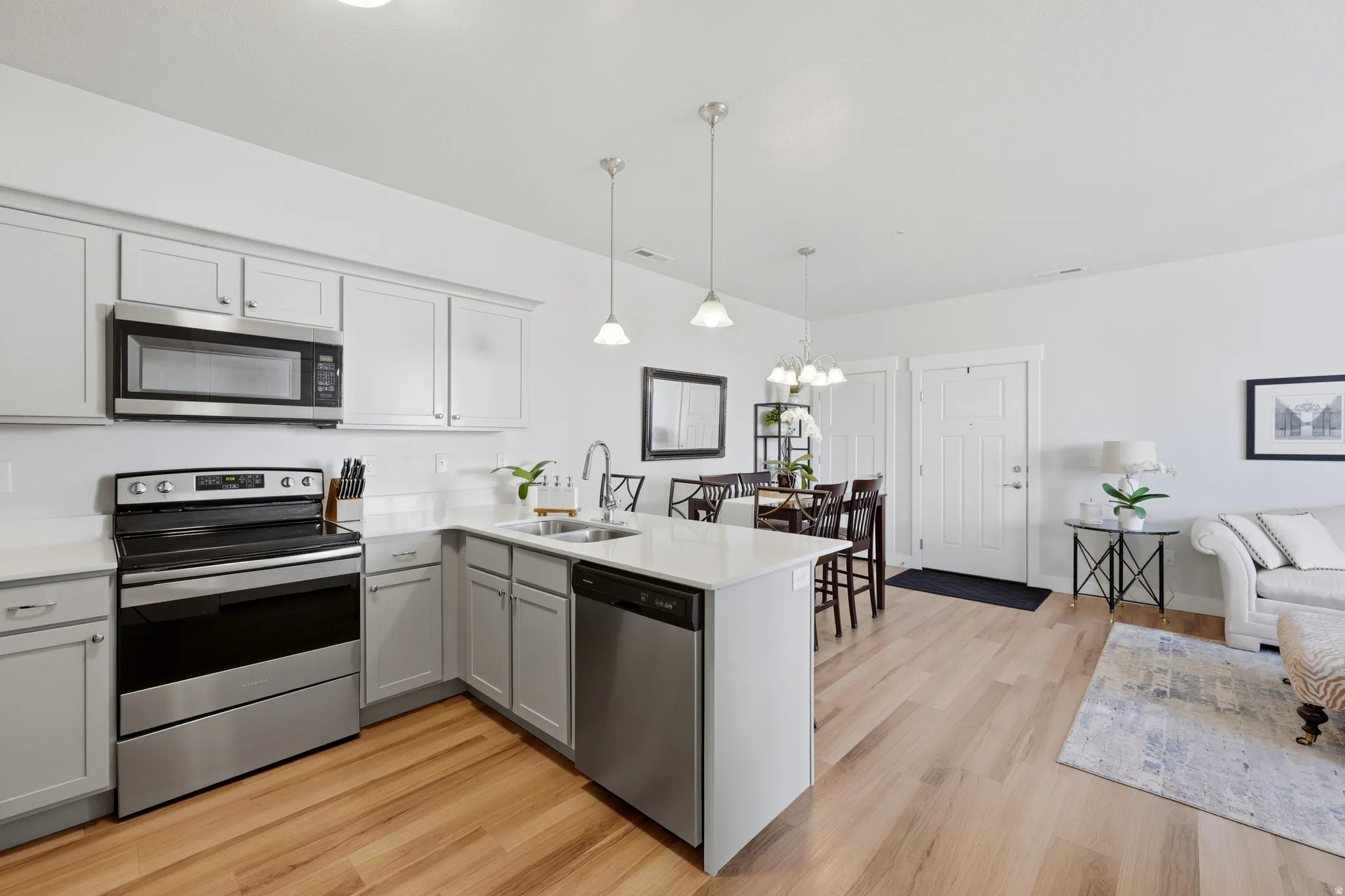 Open-concept kitchen and dining area featuring stainless steel appliances, white cabinetry with hardware accents, a large island with seating, pendant lighting, and wood-finish flooring throughout