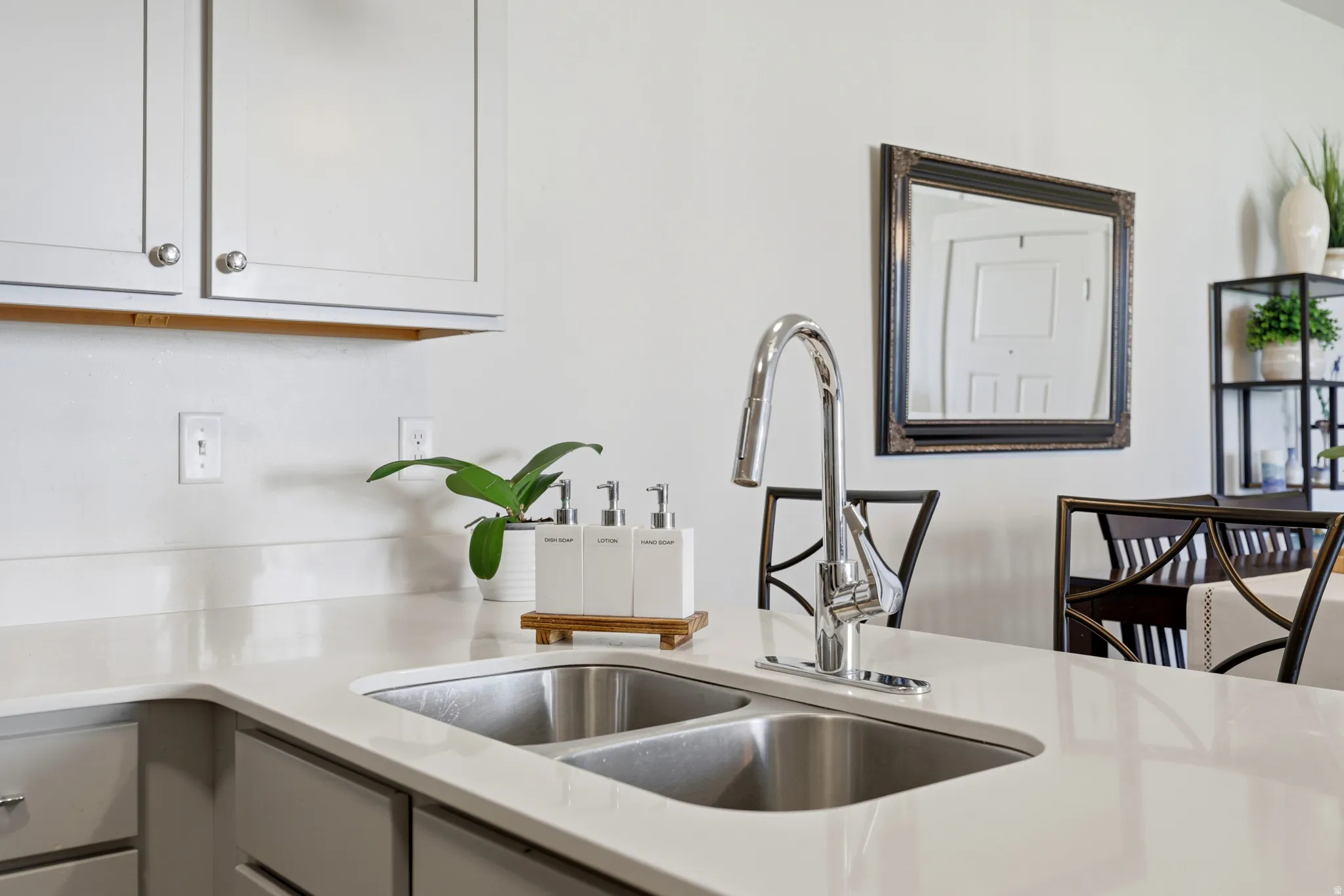 Modern kitchen featuring a stainless steel double-basin sink with a polished chrome pull-down faucet, white quartz countertops, white cabinetry with chrome hardware, and a subway tile backsplash