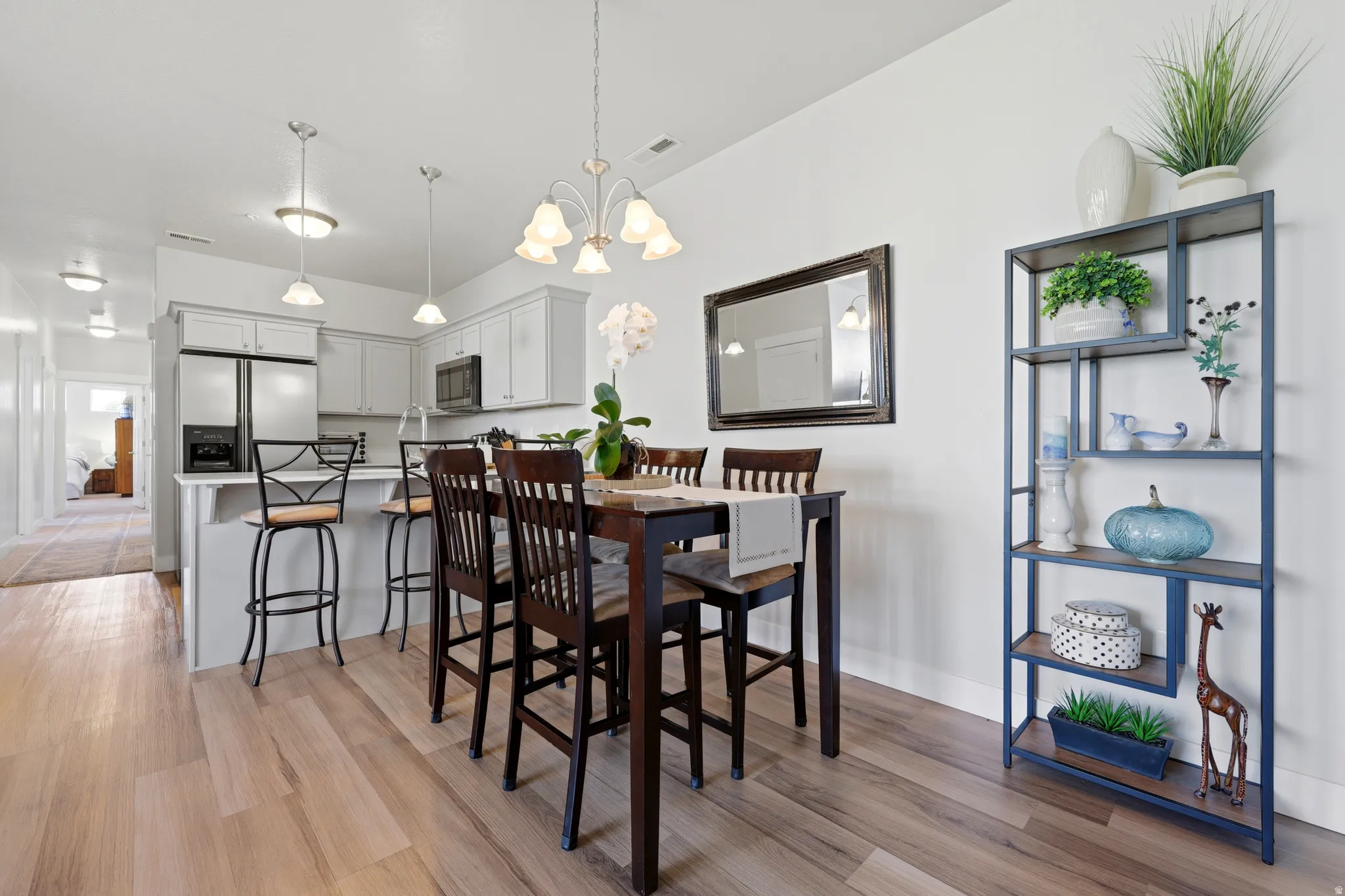 Open-concept kitchen and dining area featuring light wood-finish flooring, a contemporary chandelier, stainless steel appliances, white cabinetry, and a kitchen island with pendant lighting