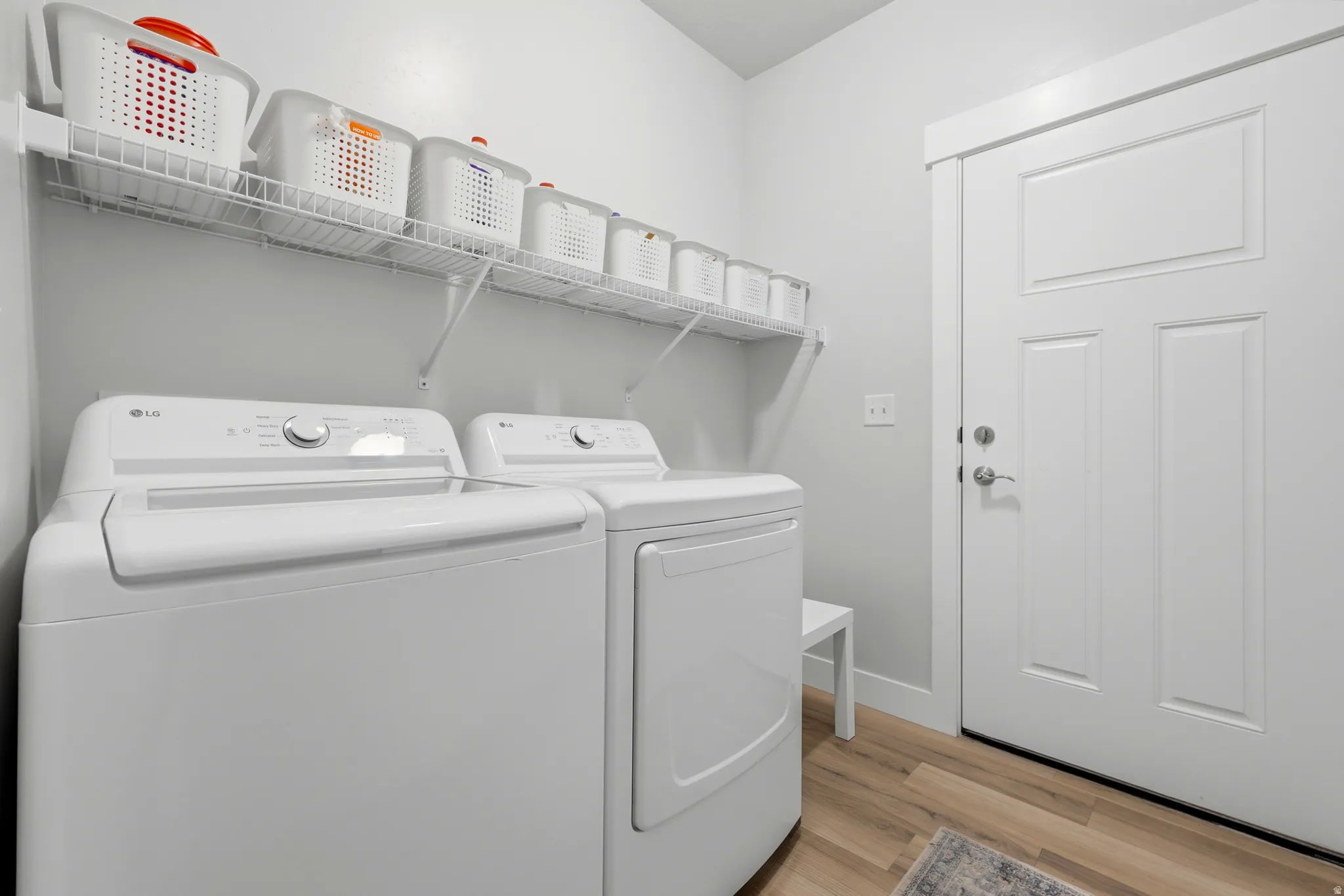 Dedicated utility area featuring a paneled door, light-toned wood-finish flooring, and a built-in wire shelving system