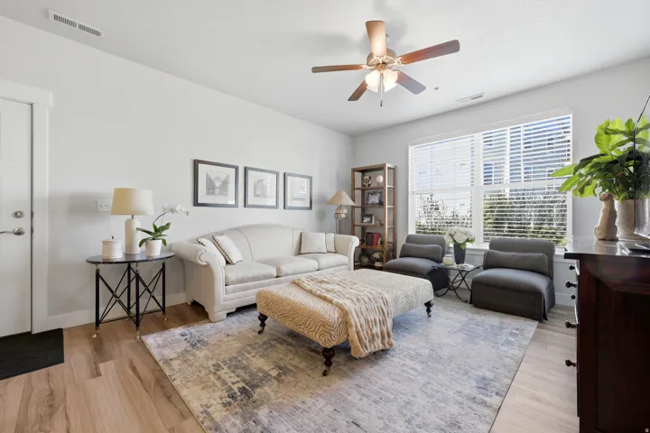 Spacious living area featuring light wood-finish flooring, a contemporary area rug, and a ceiling fan with integrated lighting