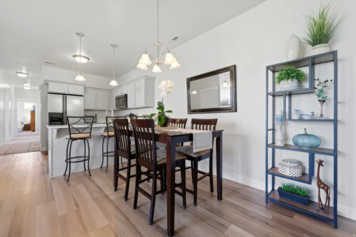 Open-concept kitchen and dining area featuring light wood-finish flooring, a contemporary chandelier, stainless steel appliances, white cabinetry, and a kitchen island with pendant lighting