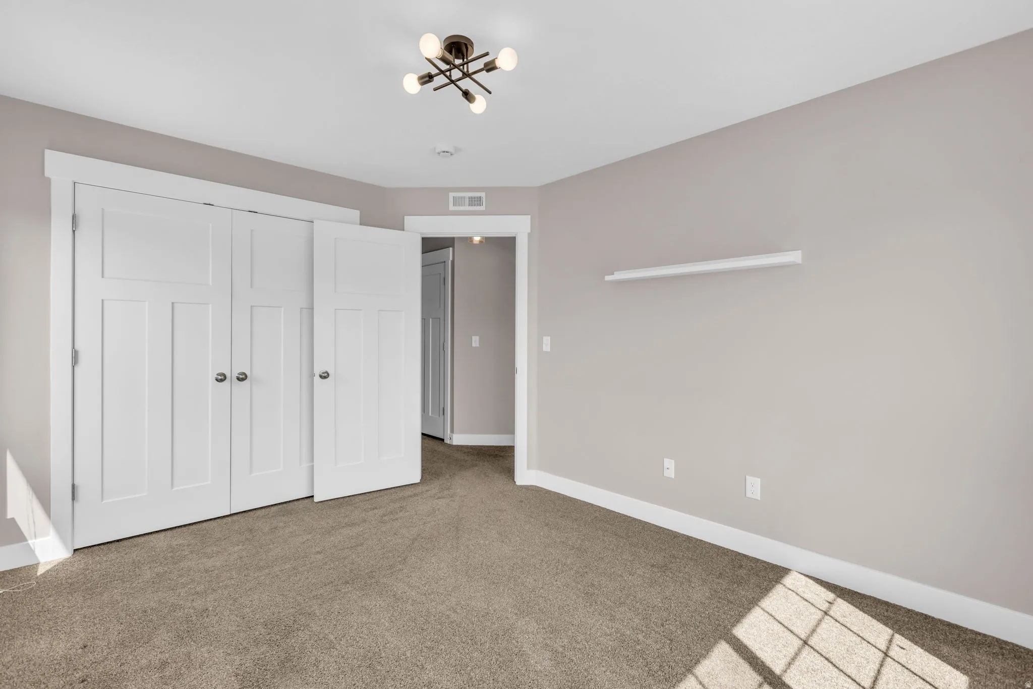 Neutral-toned room featuring a multi-panel bifold closet door, plush carpet flooring, and a modern ceiling light fixture