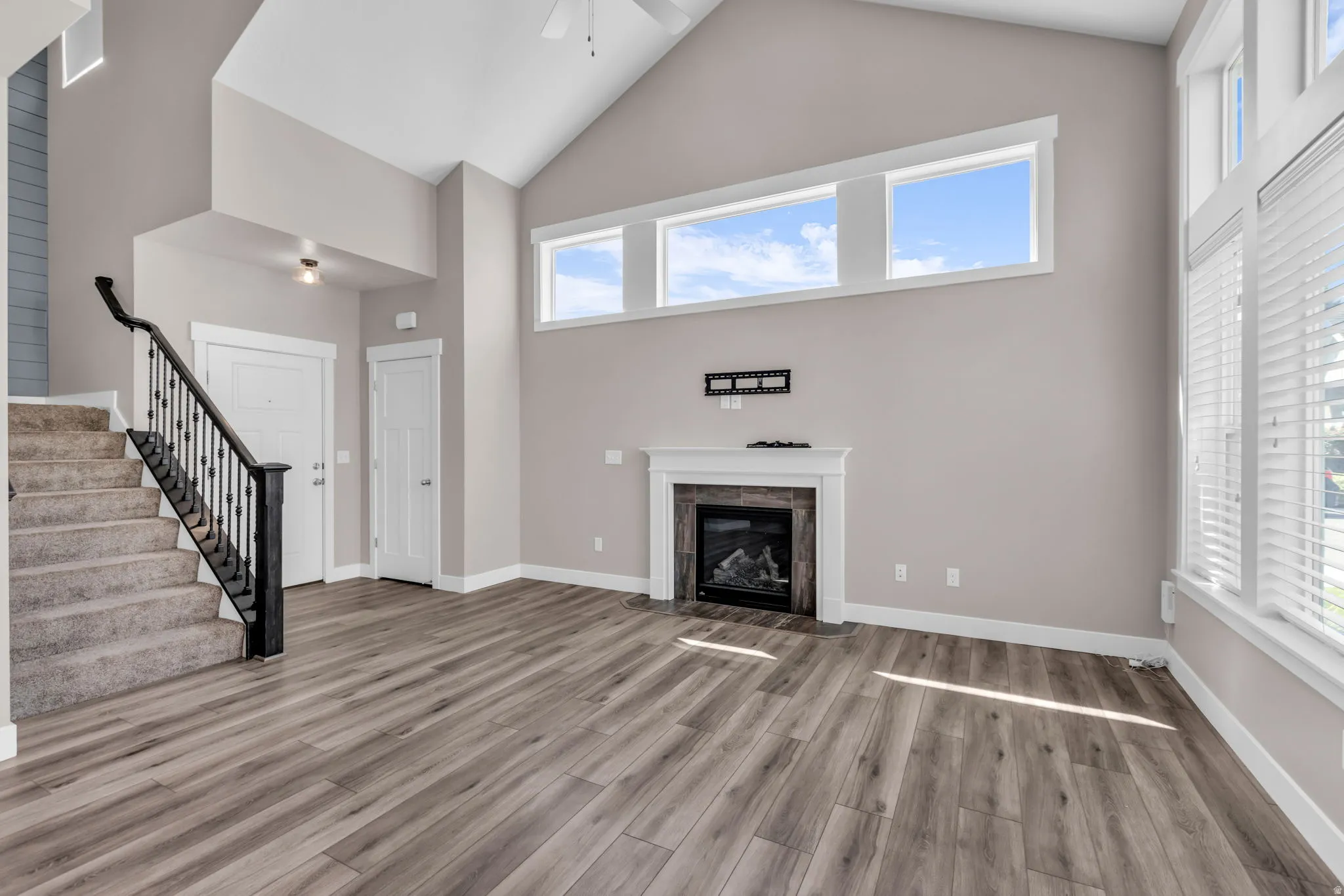 Bright and open great room showcasing vaulted ceilings with skylights, wood-finish plank flooring, a fireplace with dark surround, and abundant natural light from transom windows