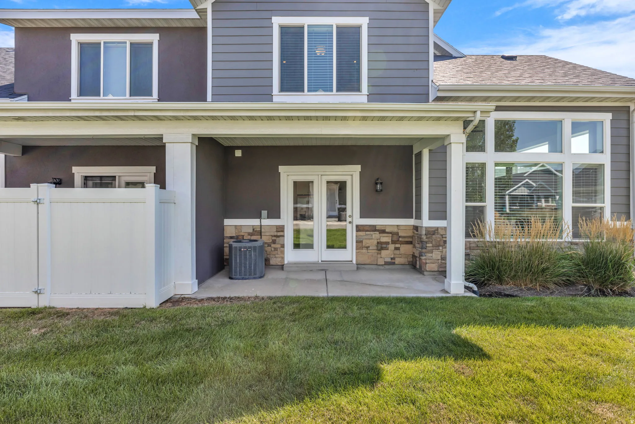 Modern two-story home featuring a covered front porch with white columns and stone accents, French doors with multi-pane glazing, and a welcoming entry
