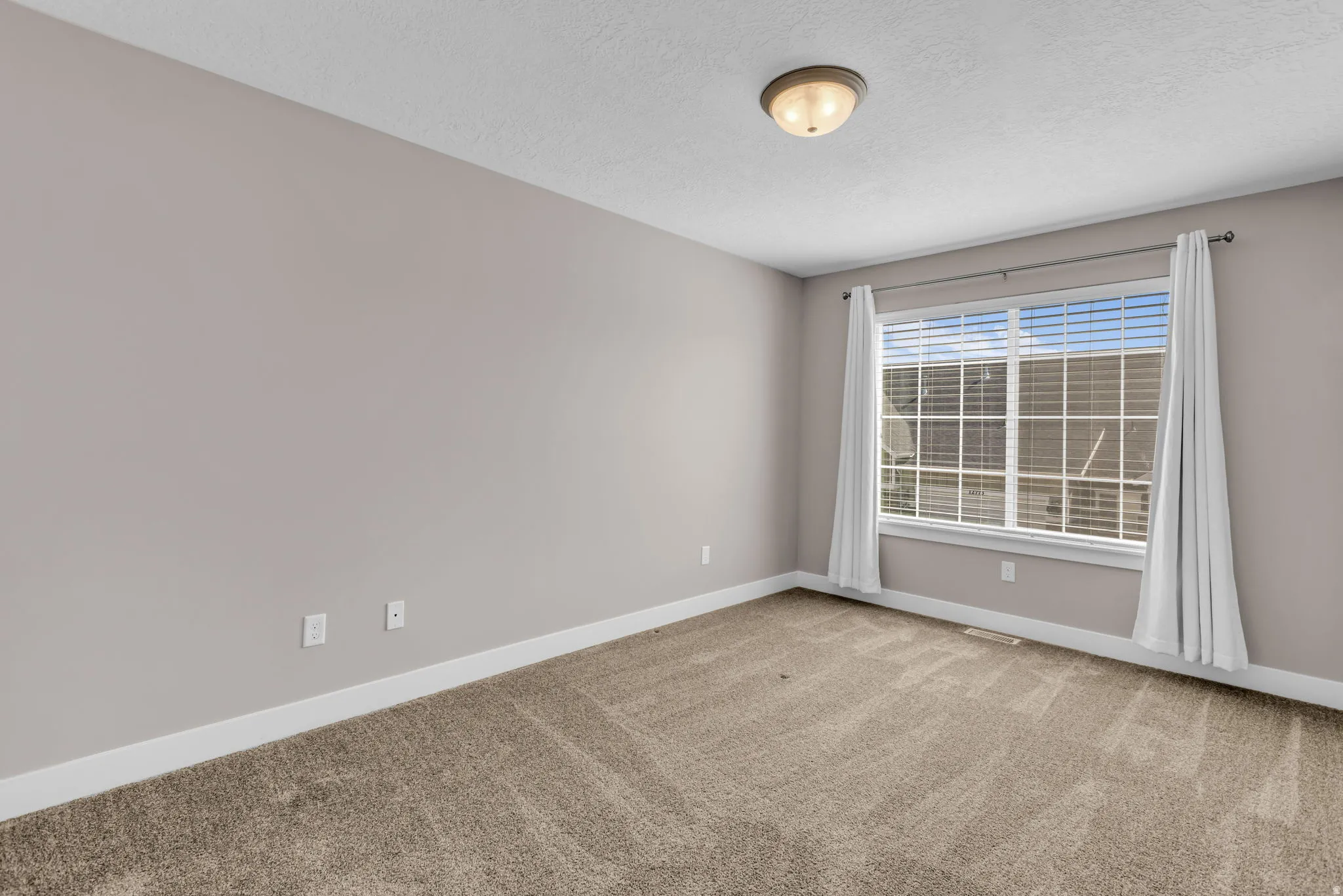 Carpeted room featuring a double window with blinds and curtains, neutral wall paint, white baseboards, and a semi-flush mount ceiling fixture