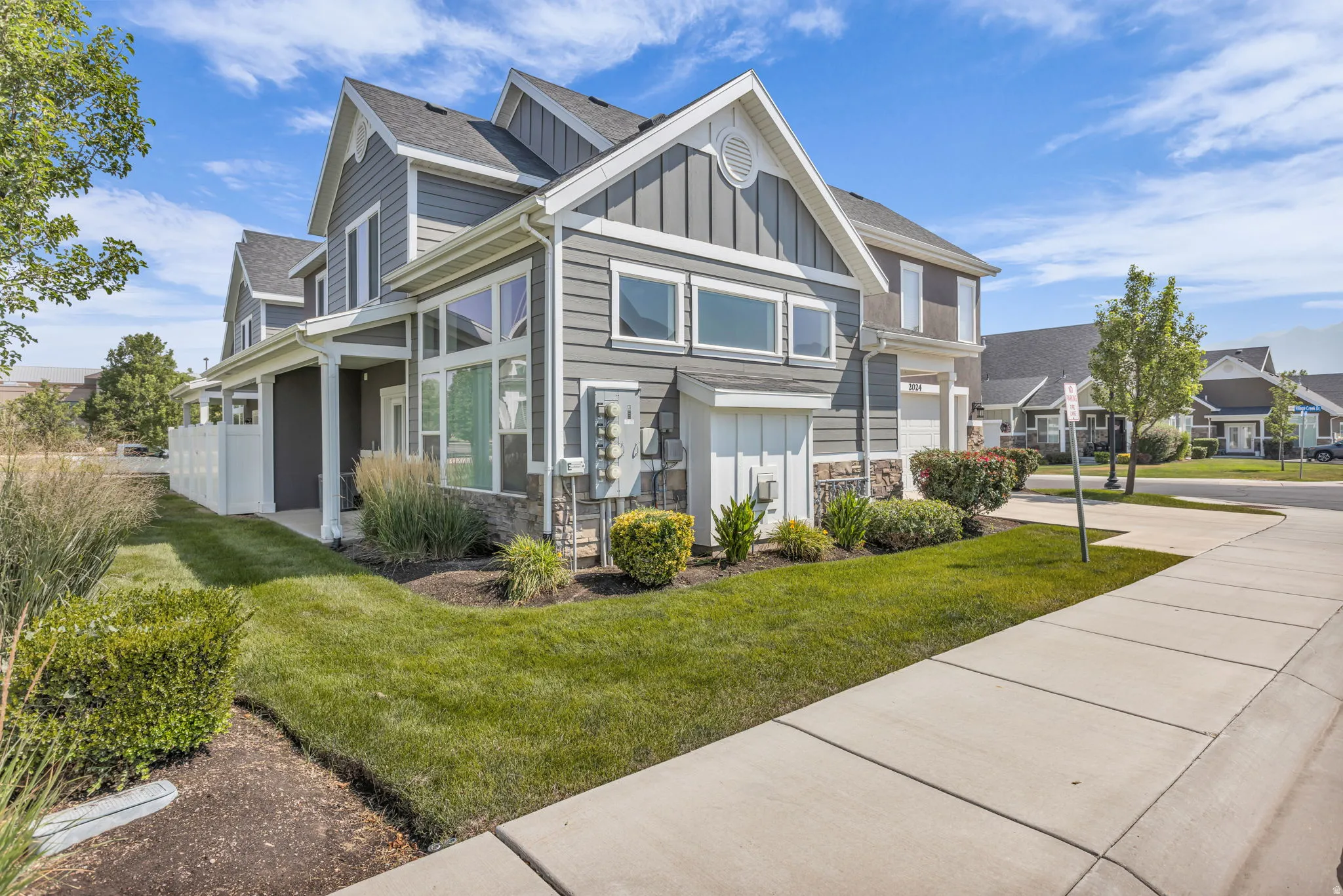 Contemporary-style residence featuring gray siding, white trim, stone accents, multiple large windows, and an attached garage