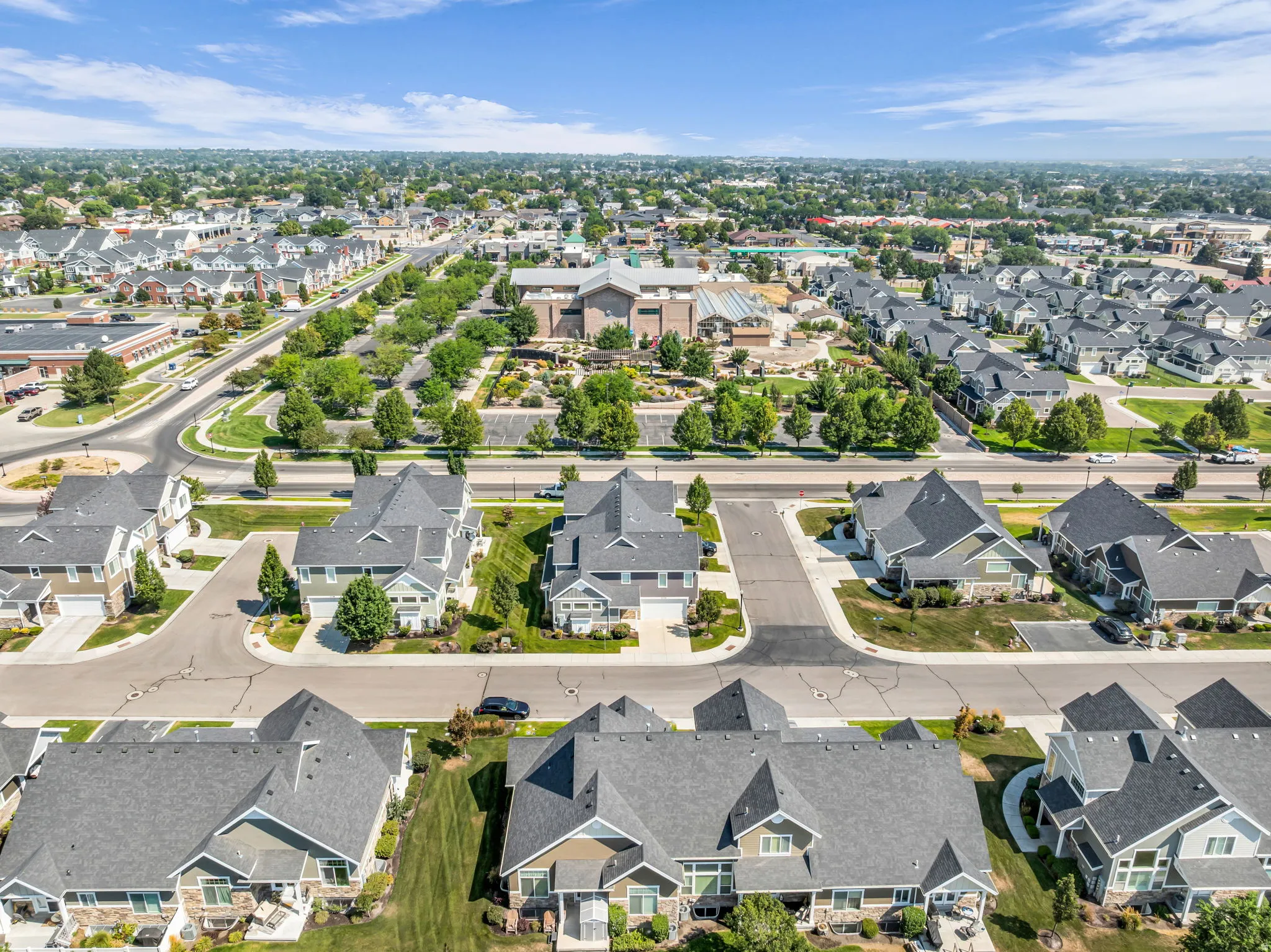 Aerial view showcasing a well-planned residential community featuring tree-lined streets, distinctive architectural styles with varied rooflines and dark asphalt shingles, manicured lawns, and mature landscaping throughout the neighborhood