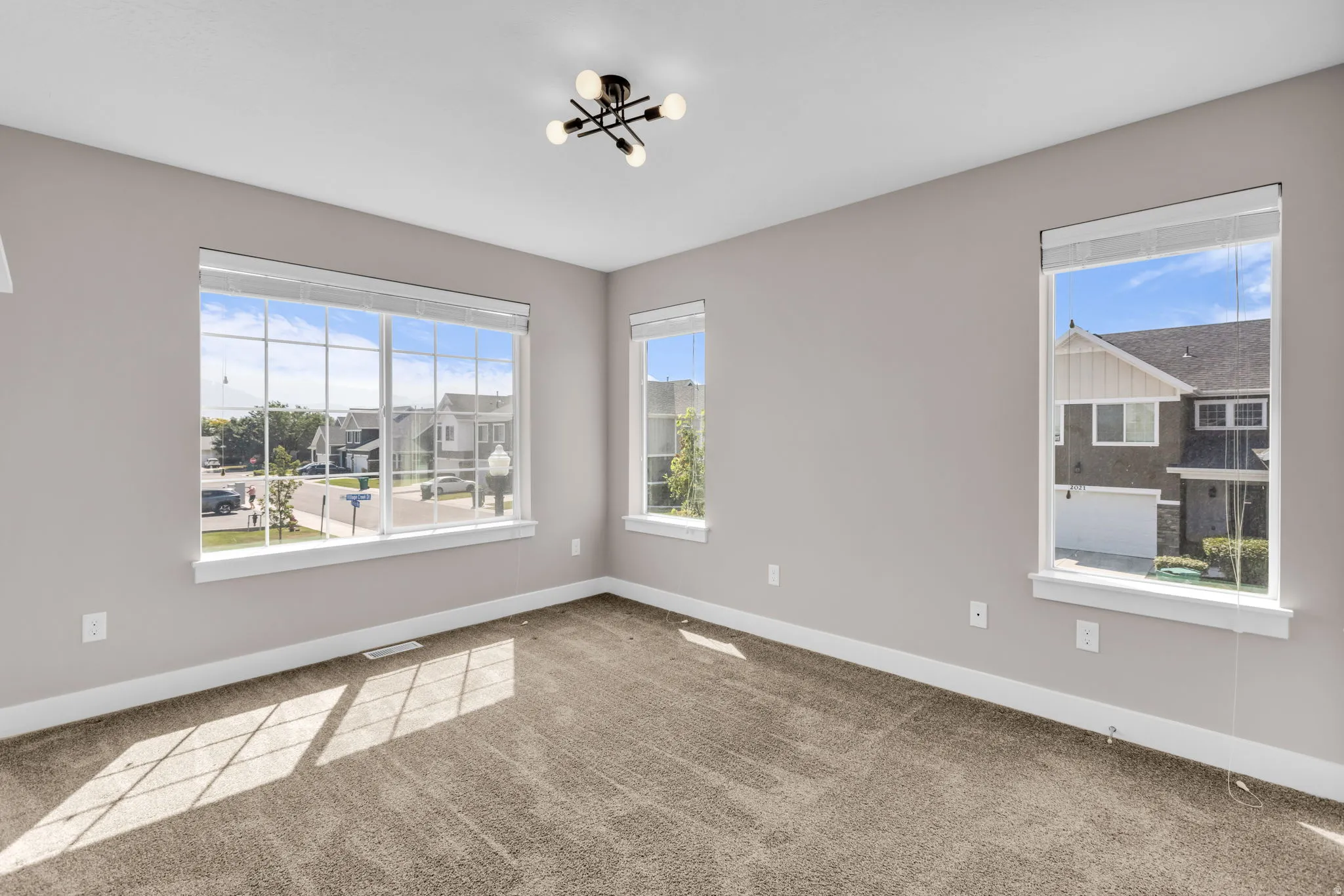 Spacious room featuring multiple windows with white trim, gray painted walls, and textured carpet flooring