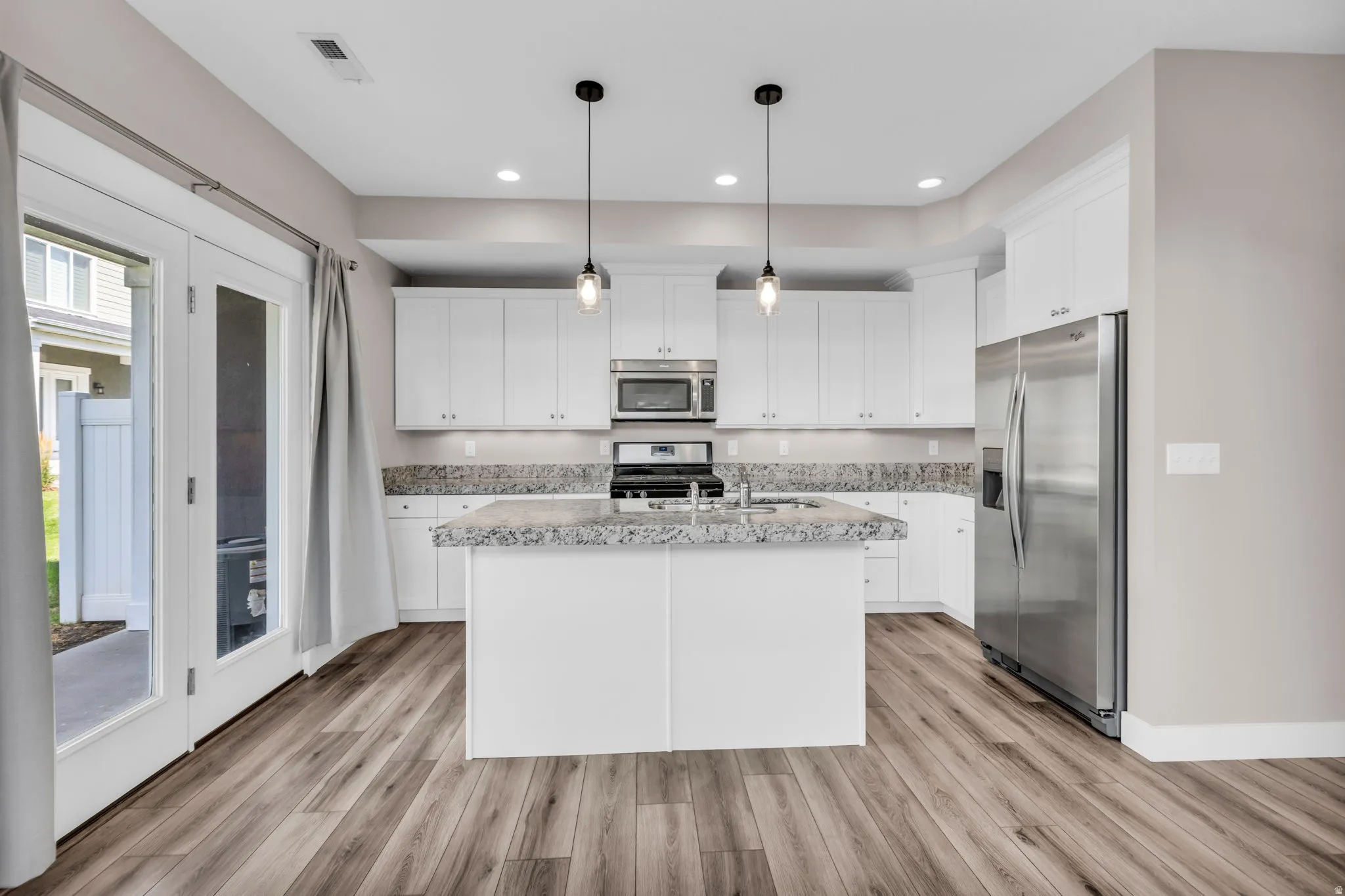 Modern kitchen featuring white cabinetry, stainless steel appliances, and a central island with a stone-finish countertop
