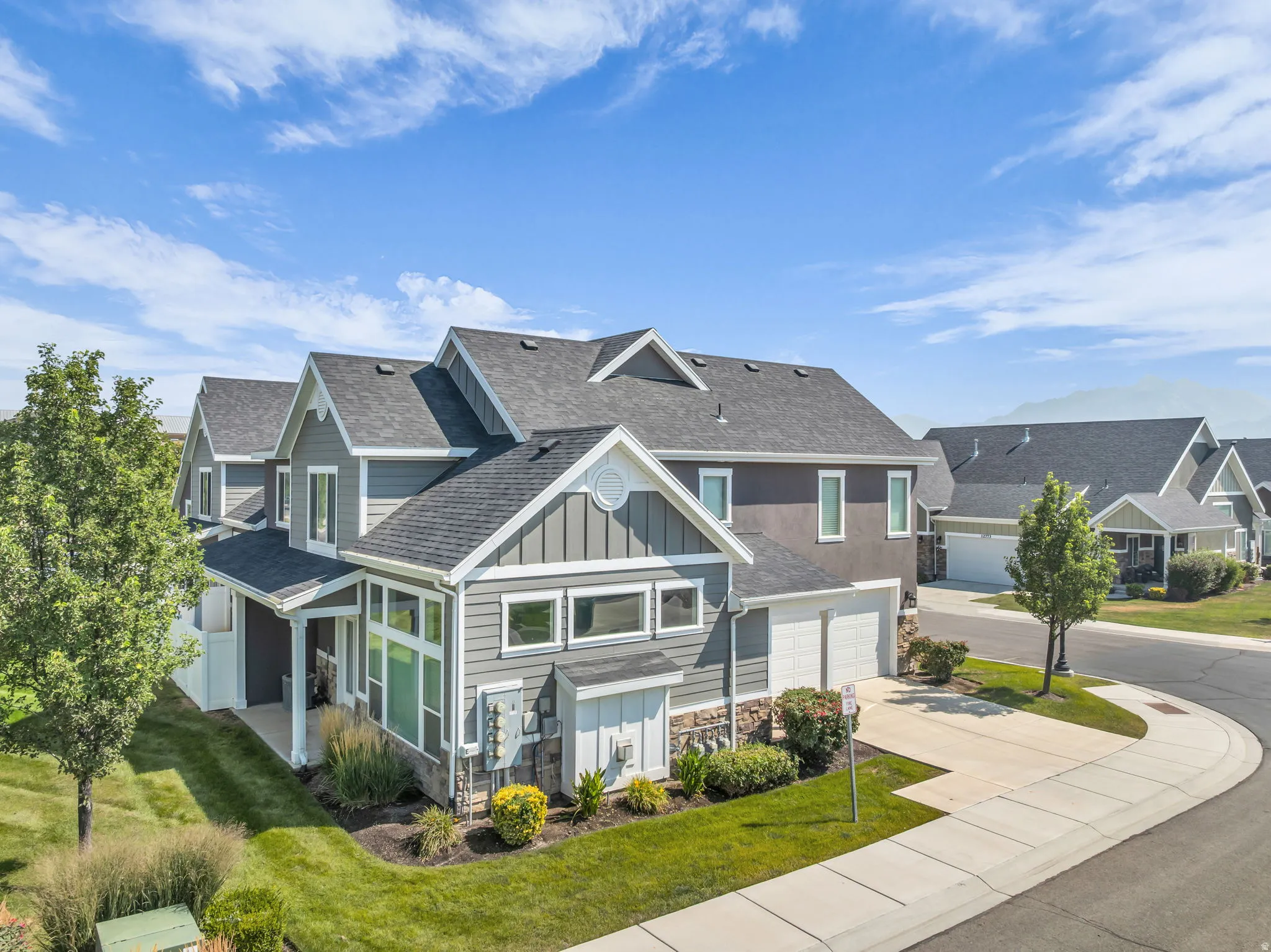 Contemporary residential property featuring a gray facade, white trim, attached two-car garage, manicured lawn, and paved driveway