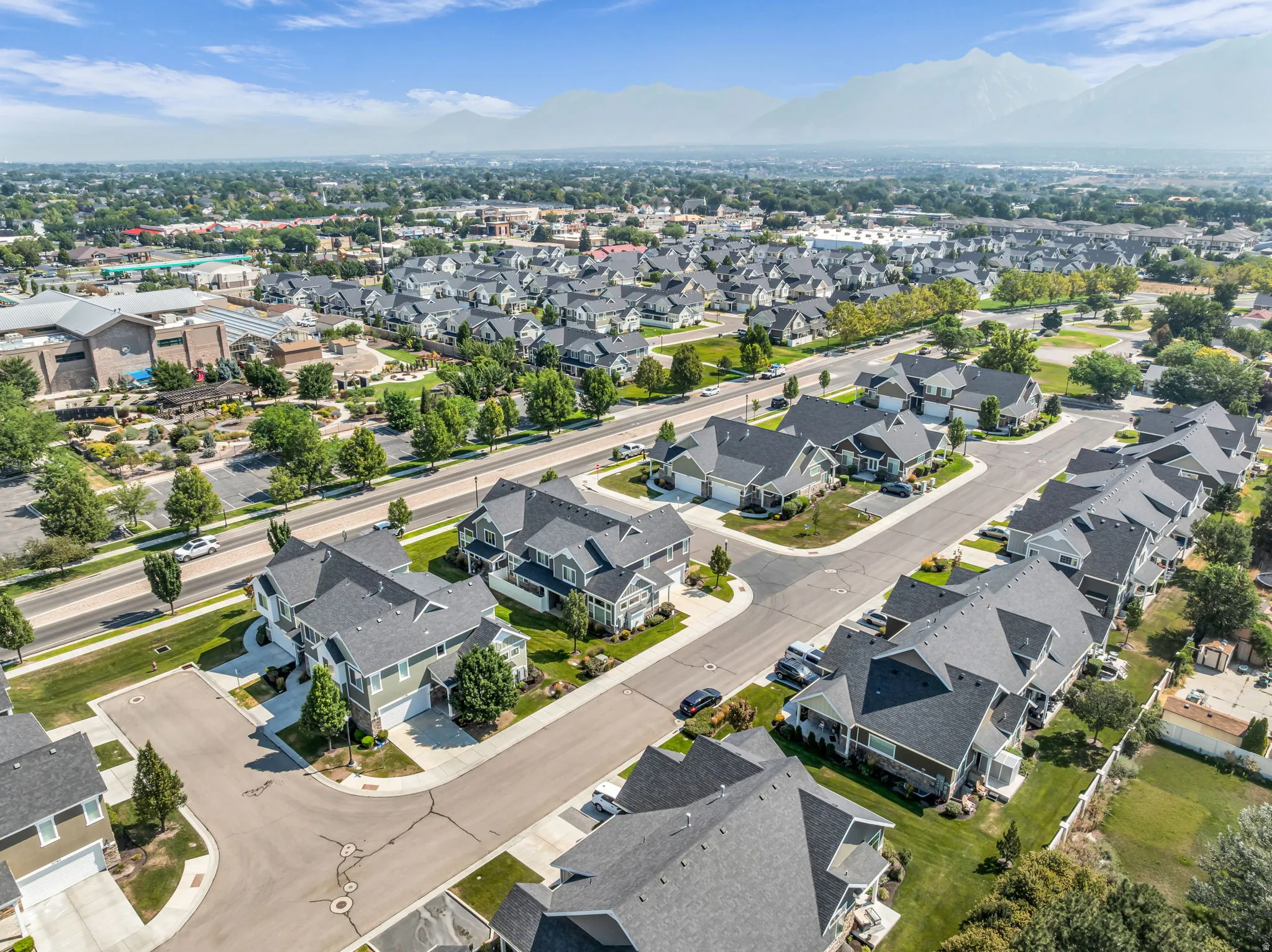 Prestigious residential community featuring elegant two-story homes with dark architectural roofing, manicured lawns, mature landscaping, and wide tree-lined streets